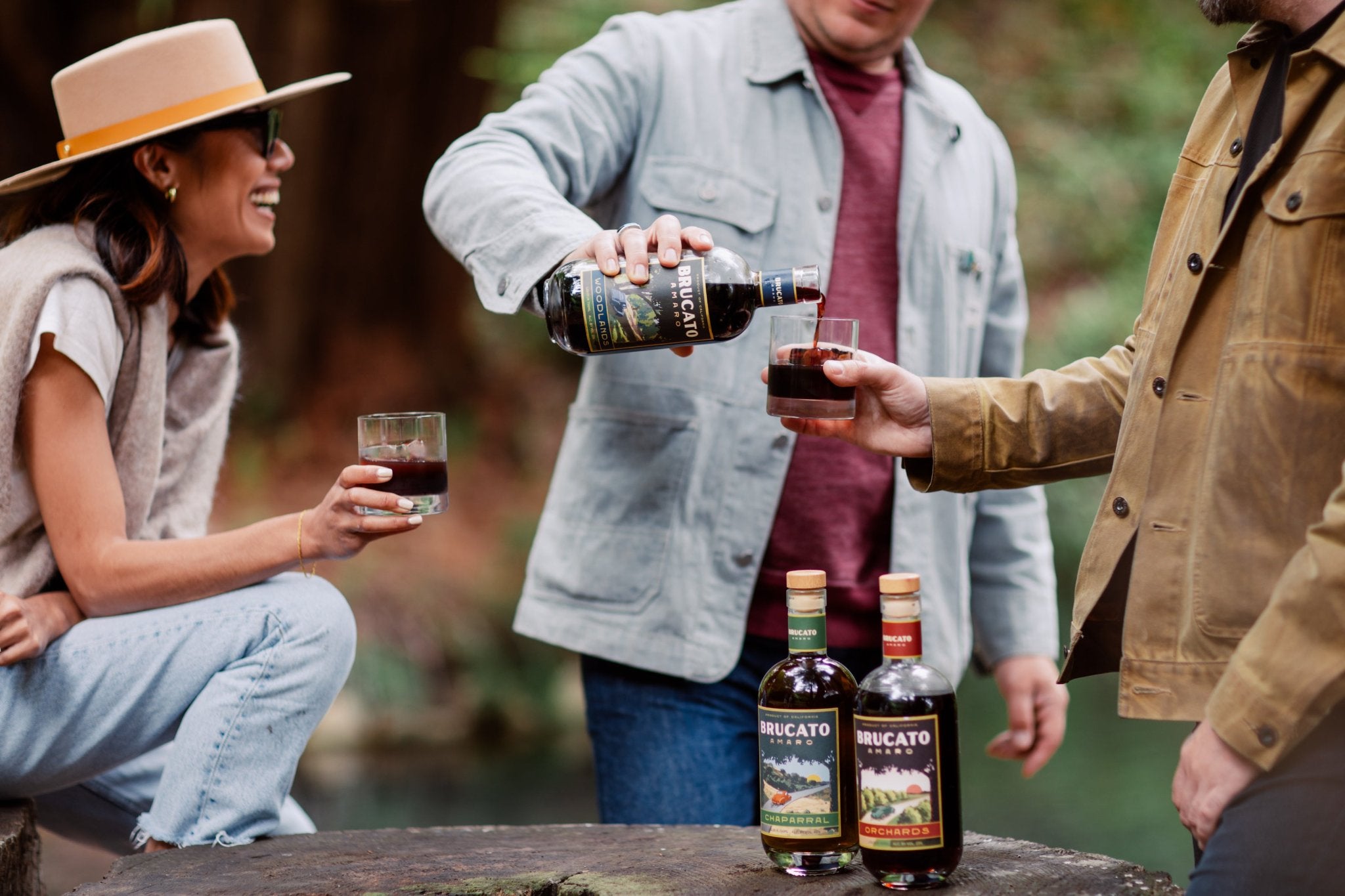 Three friends in the forest pouring Brucato Amaro cocktails and laughing.