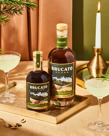 Bottles of Brucato Amaro Chaprral on a table with cocktails and snacks